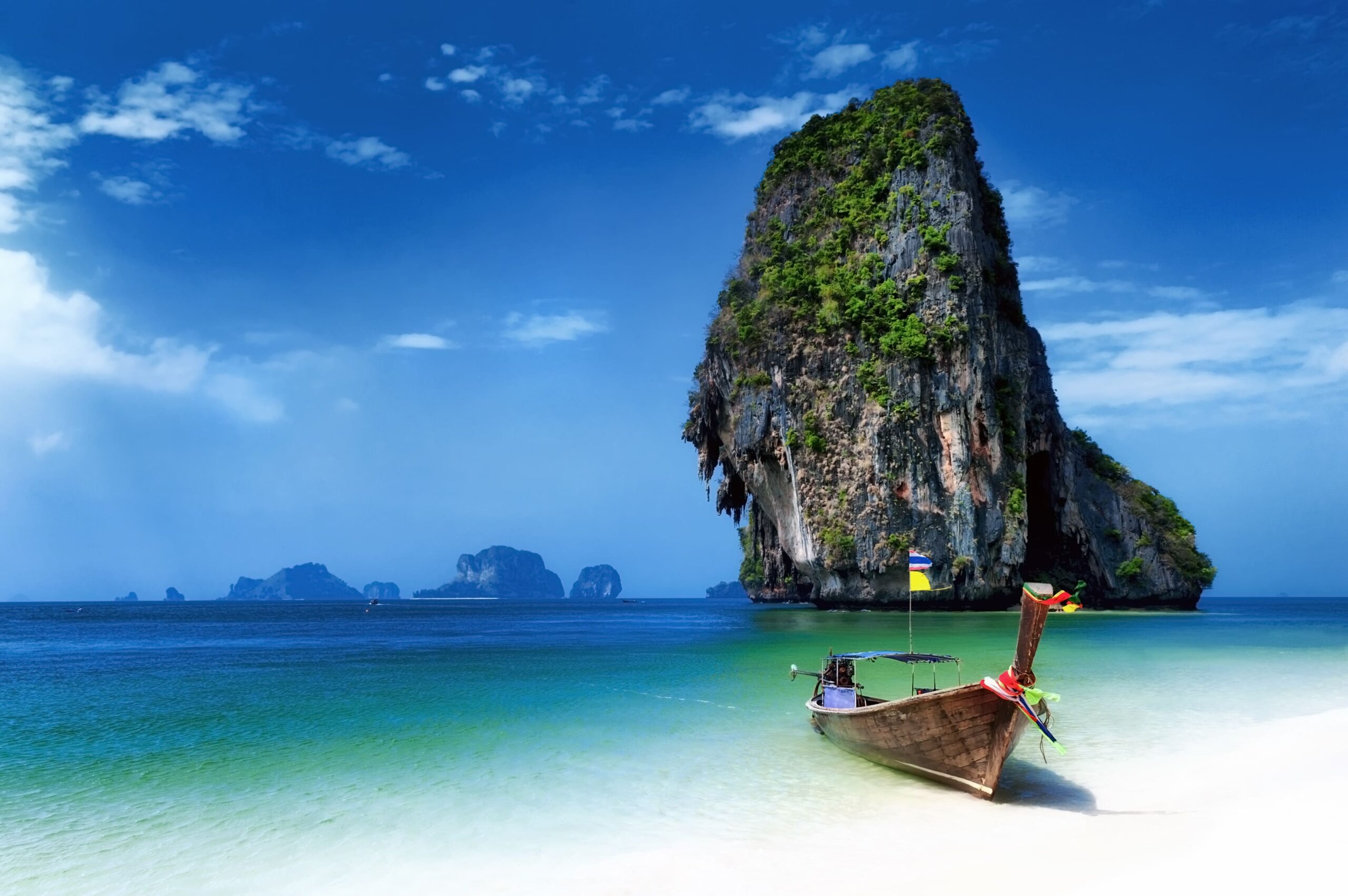 Traditional Thai longtail boat on a white sand beach with turquoise water and a towering limestone karst offshore.