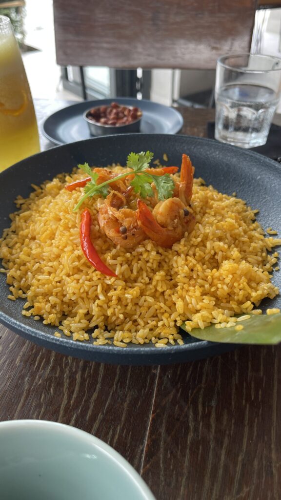Shrimp fried rice with chilies Plate of golden fried rice topped with shrimp, red chilies, and cilantro on a wooden café table.
